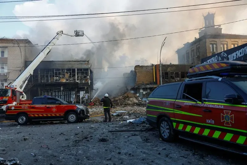 دخان يتصاعد من مبنى مدمر في كييف بعد هجوم بطائرات مسيرة، بينما رجال الإطفاء يعملون على إخماد النيران.