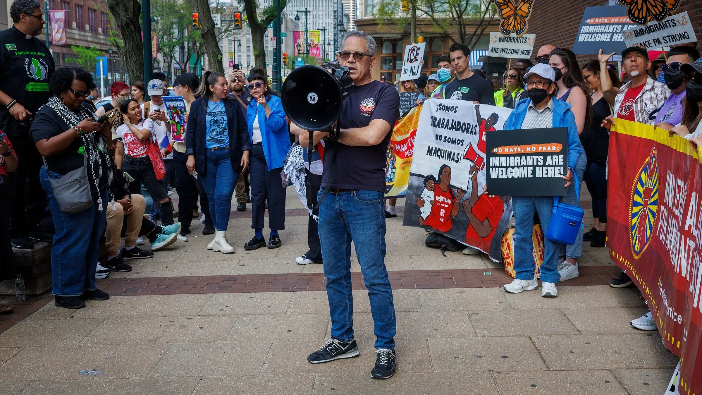 تجمع حاشد في فيلادلفيا لدعم المهاجرين، حيث يتحدث رجل عبر مكبر صوت وسط لافتات تعبر عن الترحيب بالمهاجرين.