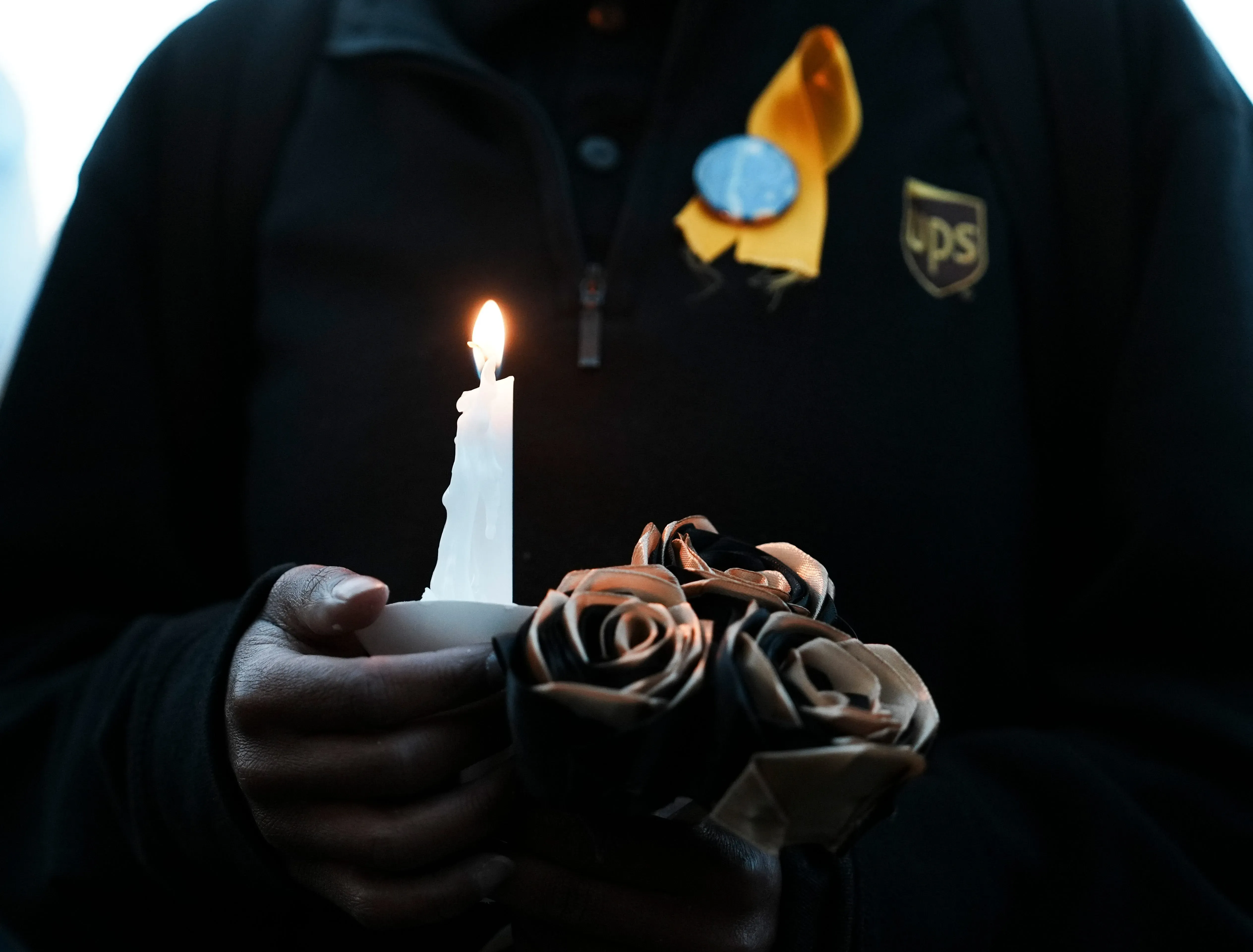 شخص يحمل شمعة مضاءة وزهورًا سوداء، يعبر عن الحزن بعد حادث تحطم طائرة UPS في لويزفيل، مما أدى إلى خسائر بشرية كبيرة.