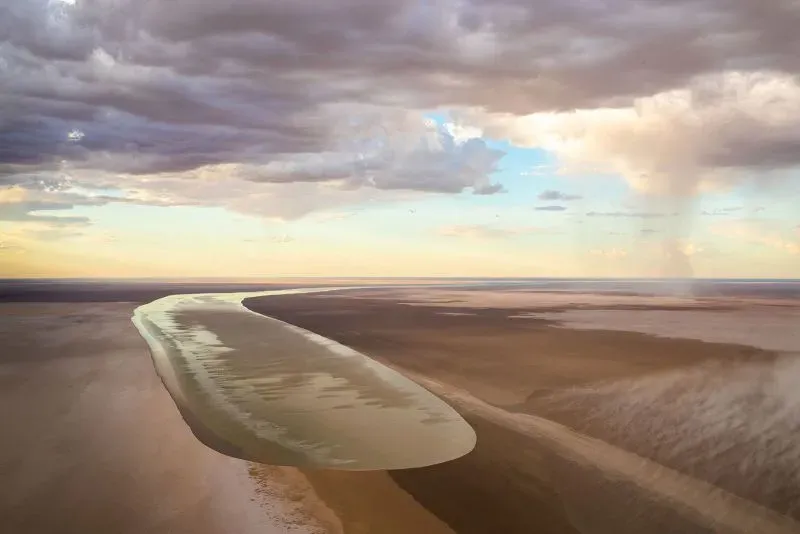 تظهر صورة بحيرة كاتي-ثندا آير في أستراليا، حيث تتدفق المياه عبر الصحراء، محاطة بسحب كثيفة، مما يعكس حدثًا نادرًا يجذب الحياة البرية والسياح.