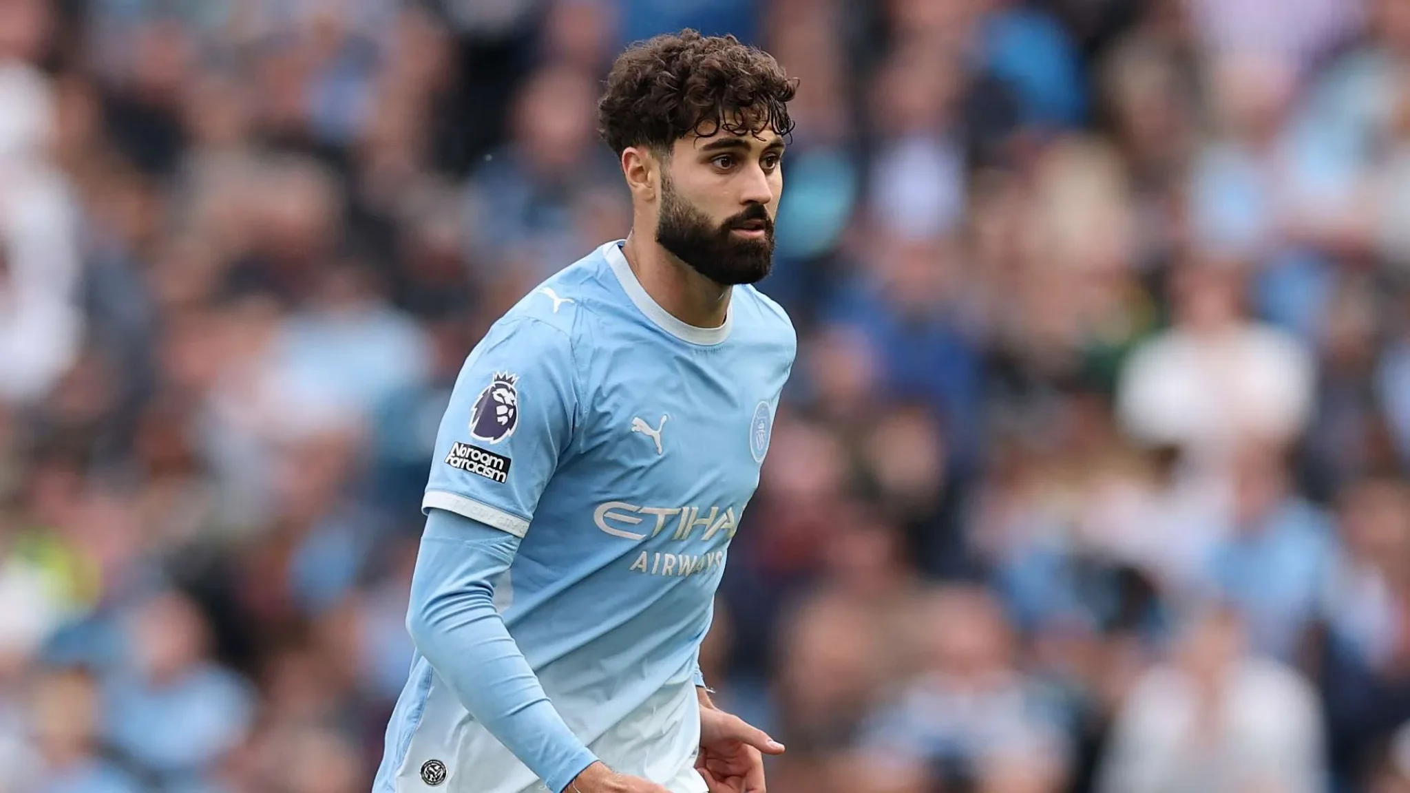 لاعب مانشستر سيتي بيرناردو سيلفا يرتدي الزي الأزرق خلال مباراة في الدوري الإنجليزي الممتاز وسط جمهور غامض.