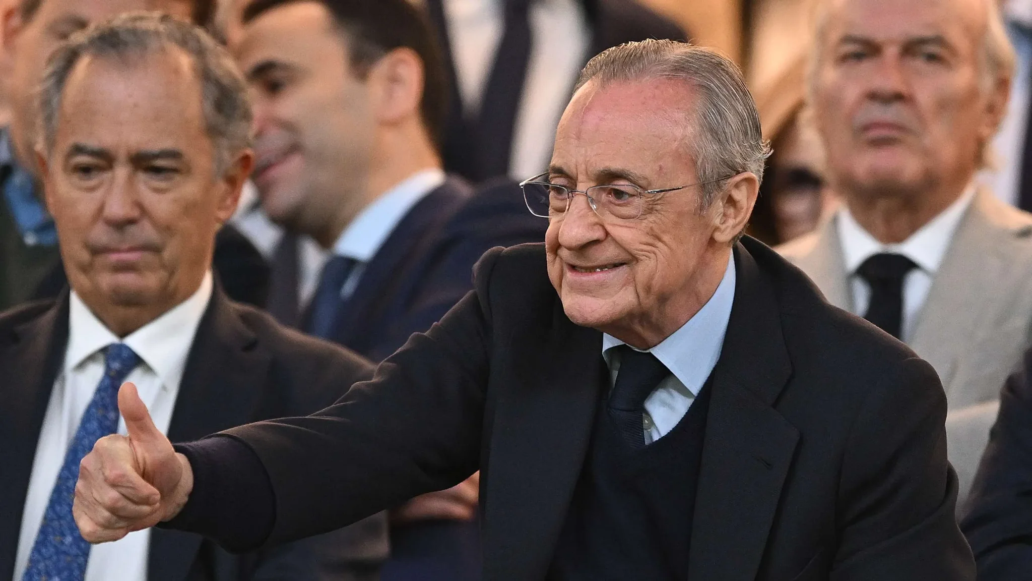 فلورنتينو بيريز رئيس ريال مدريد يظهر مبتسماً ويشير بإبهامه وسط حضور رسمي، في سياق متابعة فرص تعاقدات النادي مع لاعبين من مانشستر سيتي.