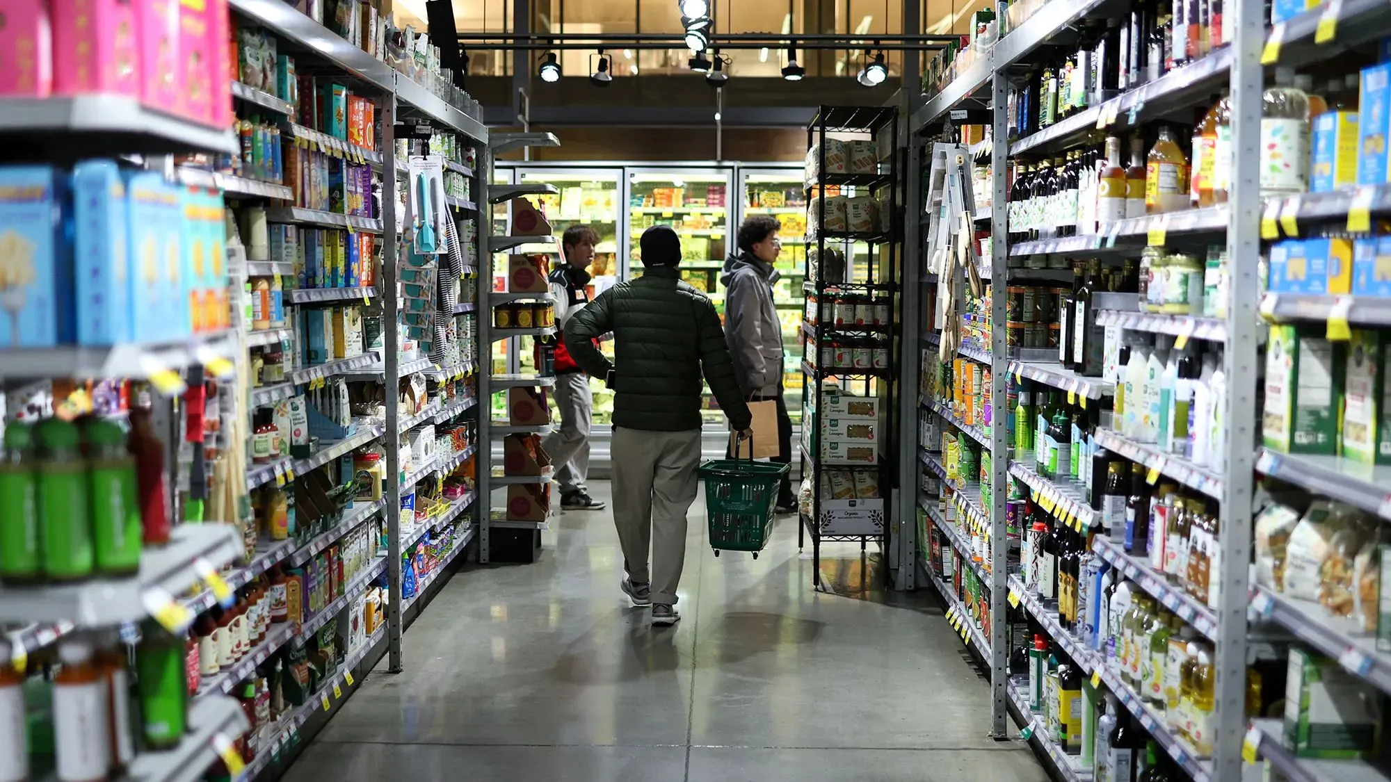 شخص يتسوق في ممر بقالة، محاطًا بأرفف مليئة بالمنتجات الغذائية، مما يعكس تأثير التغيرات الاقتصادية على إنفاق المستهلكين.