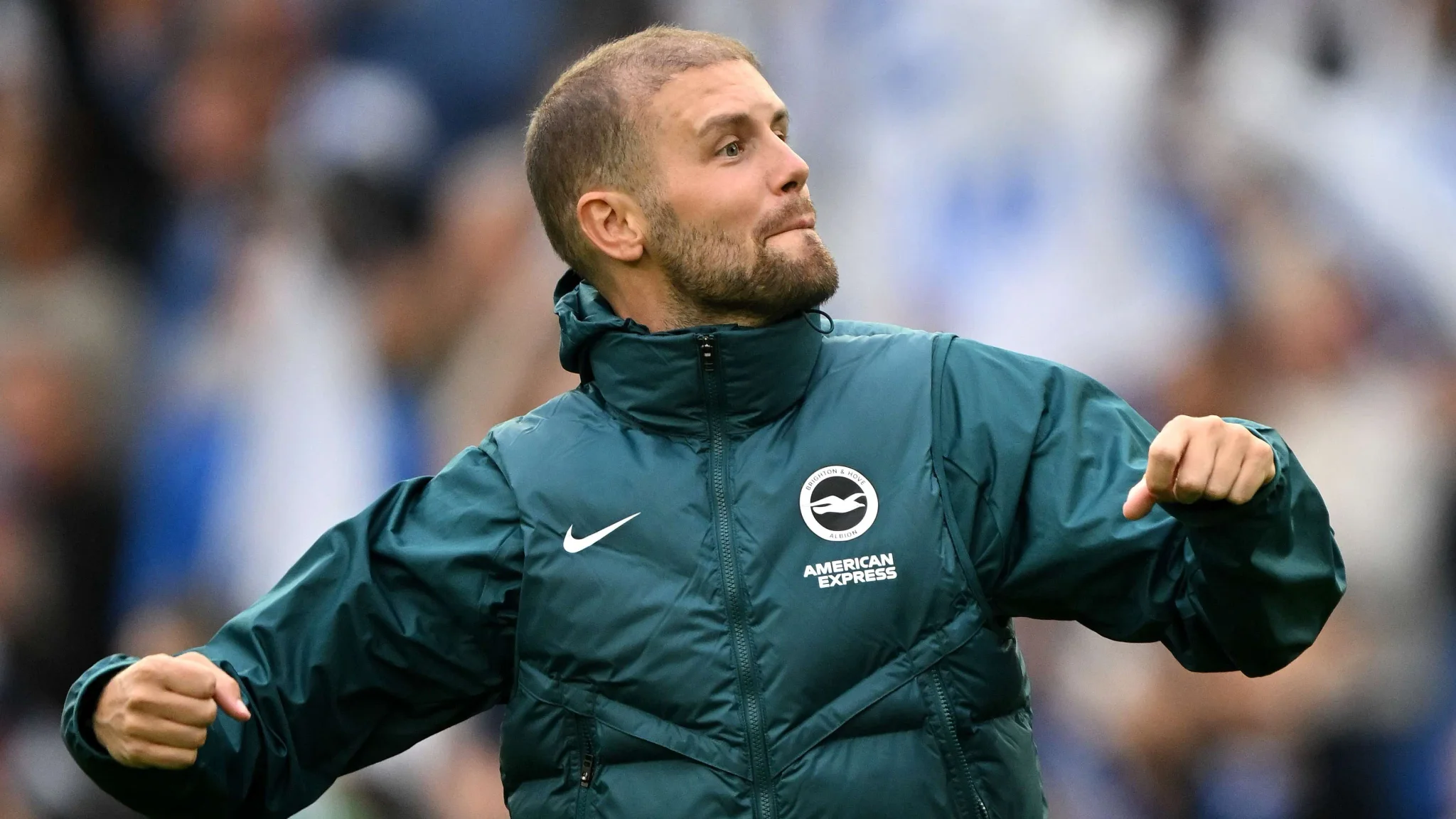 لاعب برايتون باسكال غروس يحتفل بحماس بعد تسجيل هدف في مباراة الدوري الإنجليزي الممتاز ضد أرسنال، معطف رياضي أخضر وشعار برايتون واضح.