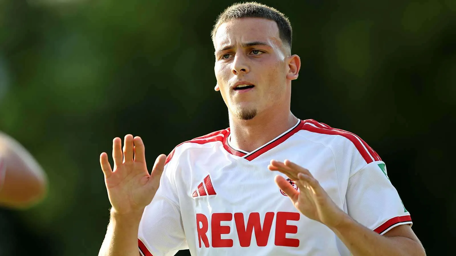لاعب كرة قدم شاب من نادي FC Cologne يرتدي قميص الفريق الأبيض أثناء التدريب، مرتبط بصفقة انتقال محتملة إلى Borussia Dortmund.