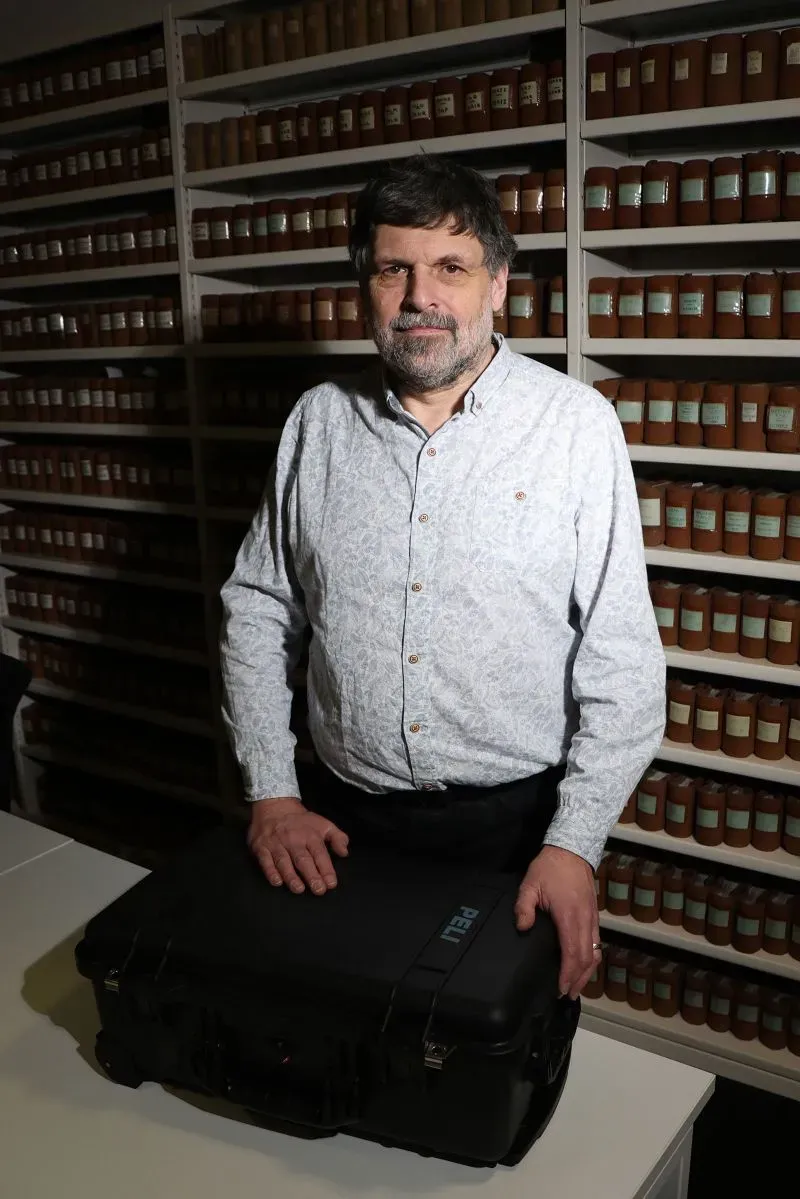 أستاذ يقف أمام مجموعة من الحاويات في مختبر، يحمل حقيبة، في سياق إعادة رفات رجل من السكان الأصليين إلى تسمانيا.