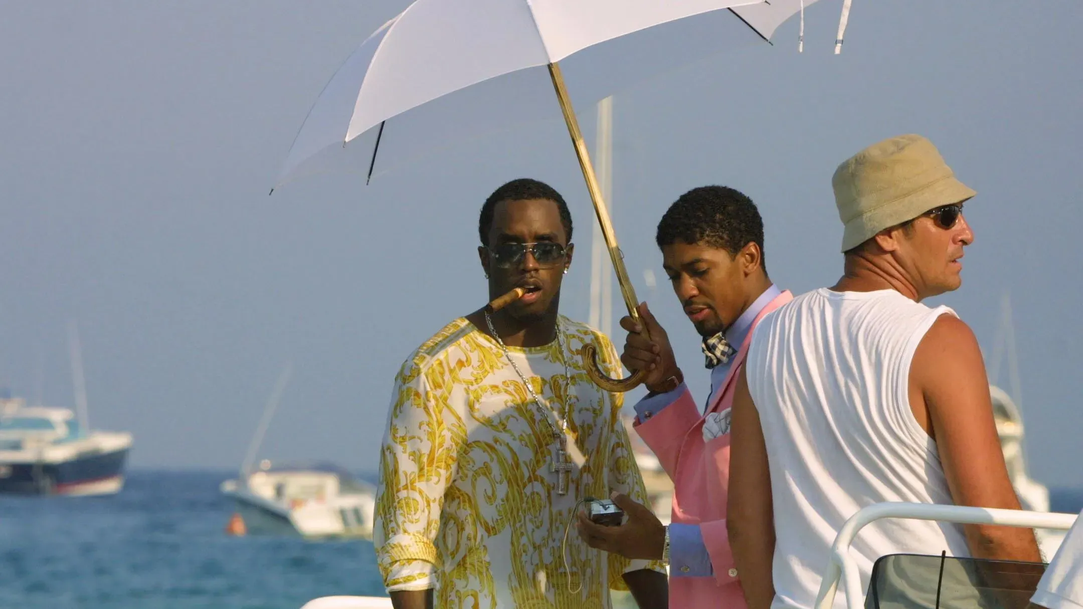 رجل يحمل مظلة لحماية شون "ديدي" كومبس من الشمس أثناء تواجدهما على متن قارب، مع شخص آخر يرتدي ملابس أنيقة.