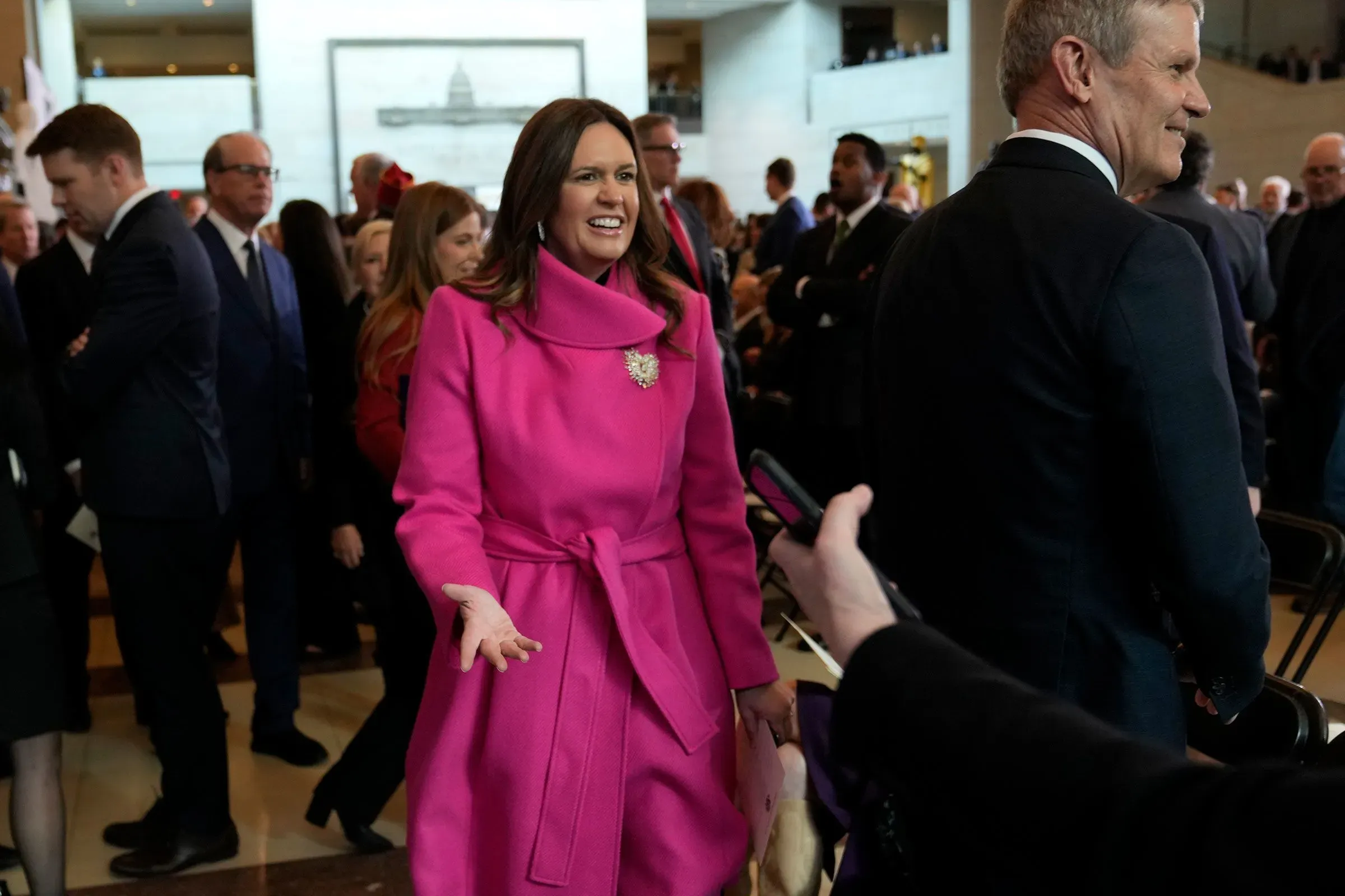 سارة هاكابي، حاكمة أركنساس، ترتدي معطفًا ورديًا وتبتسم أثناء تواجدها في حدث سياسي مع جمهور من الحضور.