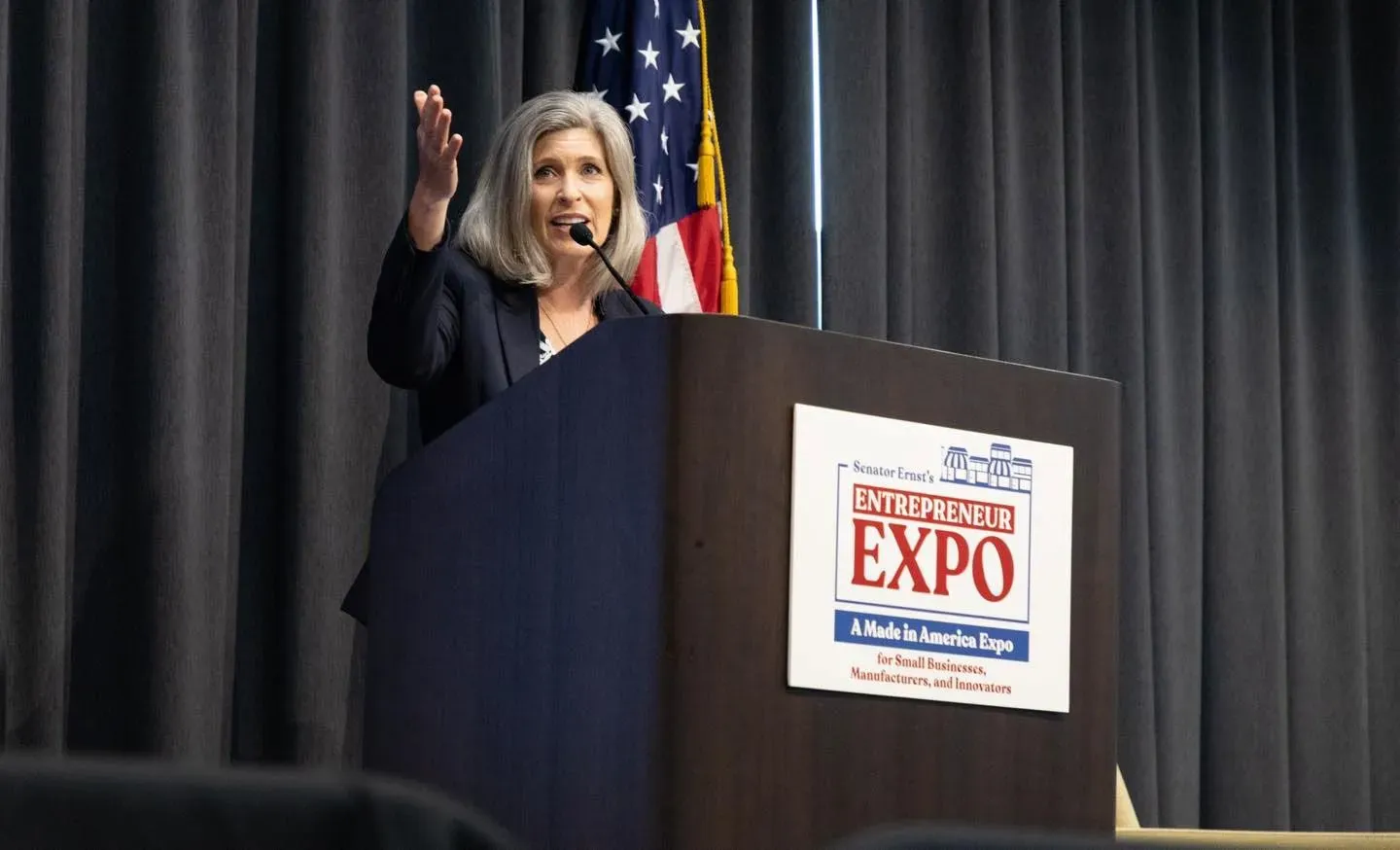 تتحدث مديرة الأعمال الصغيرة كيلي لوفلر في حدث خاص للشركات الصغيرة، مع خلفية العلم الأمريكي، حيث تناقش فرص التعاقد الفيدرالية.