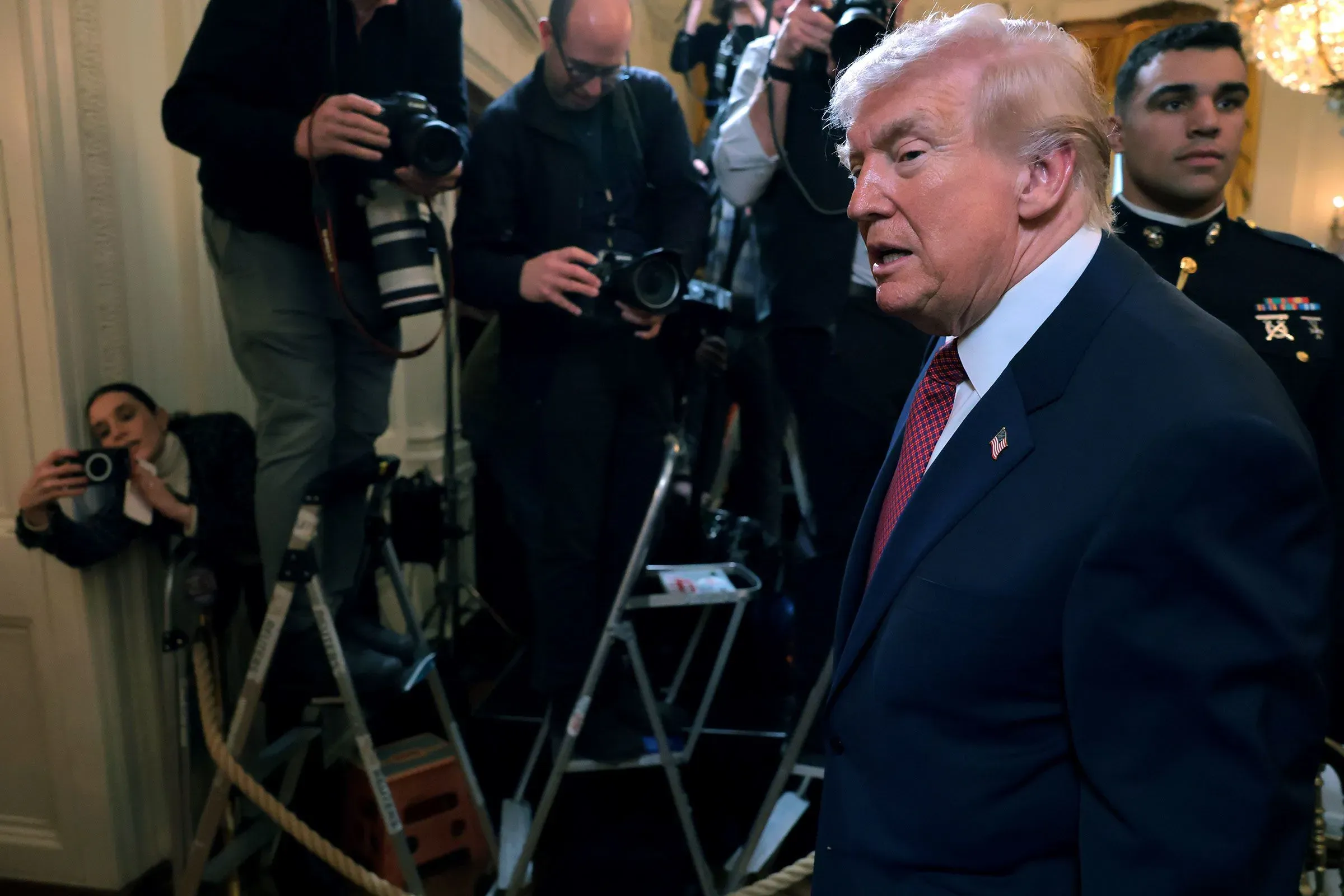 الرئيس دونالد ترامب يتحدث في حدث رسمي، محاطًا بالصحفيين والمصورين، مما يعكس الضغوط السياسية المرتبطة بقضايا الهجرة.