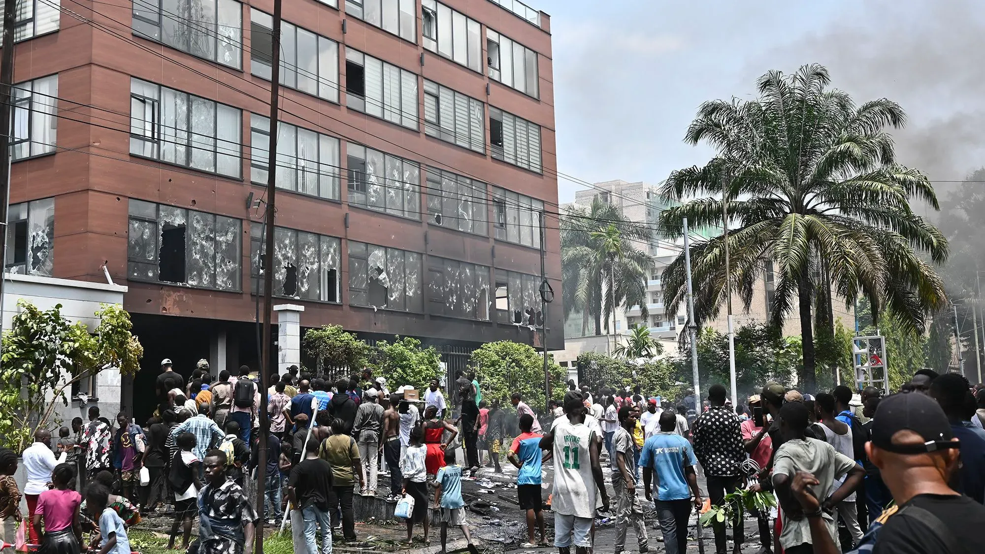 سكان غوما يتجمعون في الشارع أمام مبنى متضرر، مع تصاعد الدخان في الخلفية، خلال تصاعد العنف إثر سيطرة المتمردين على المدينة.