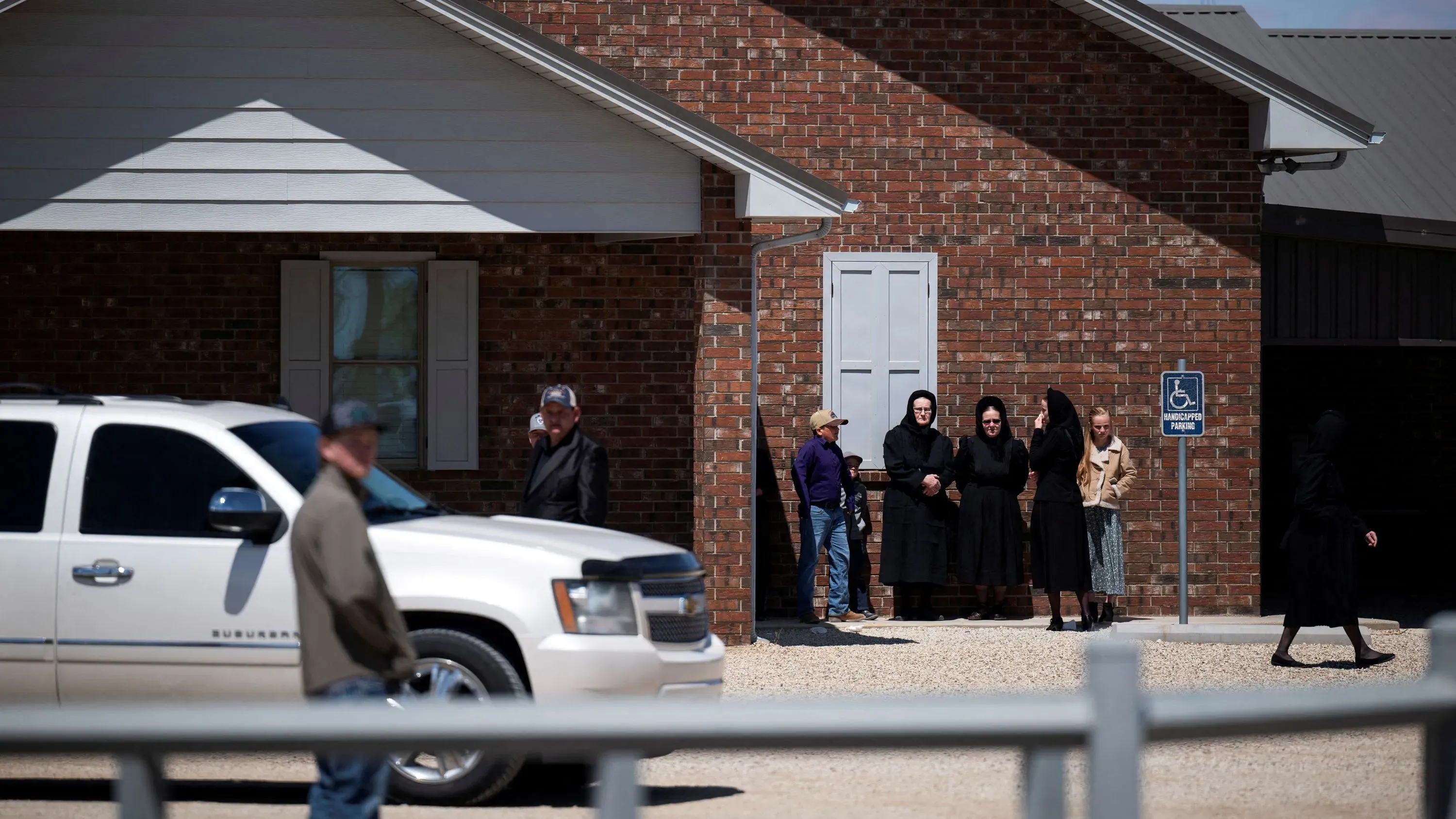 مجموعة من الأشخاص يرتدون ملابس تقليدية، يقفون أمام منزل من الطوب في ولاية تكساس، في سياق تفشي مرض الحصبة.