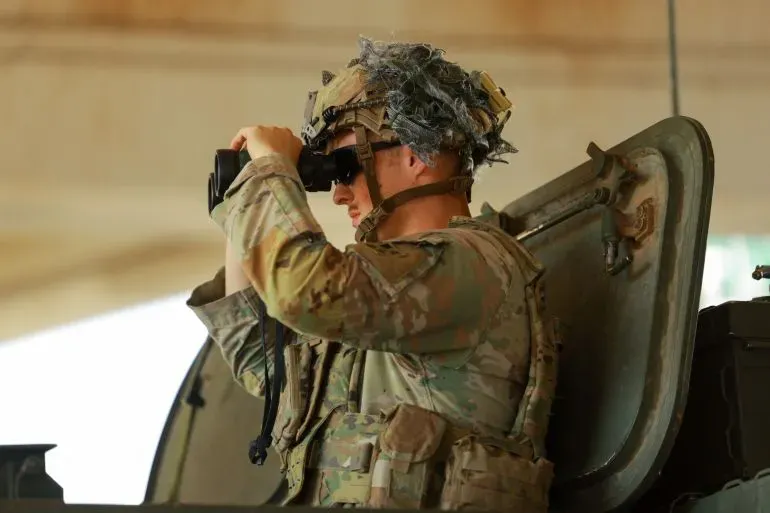 جندي أمريكي يرتدي زيًا عسكريًا، يستخدم مناظير لمراقبة منطقة معينة، في سياق التوترات حول تجارة المخدرات على الحدود المكسيكية.