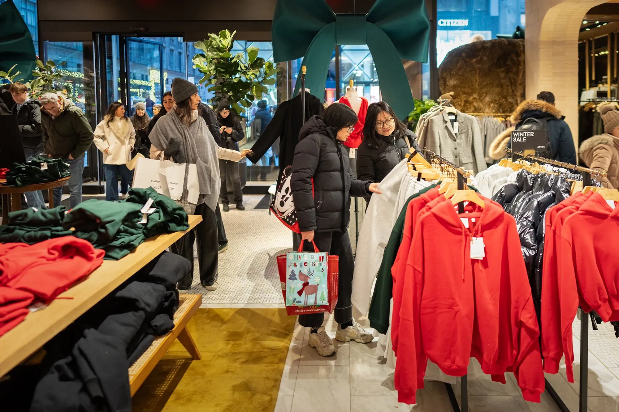 متسوقون في متجر ملابس يعاينون السلع، مع التركيز على الملابس الملونة، مما يعكس استقرار إنفاق المستهلكين في ديسمبر.