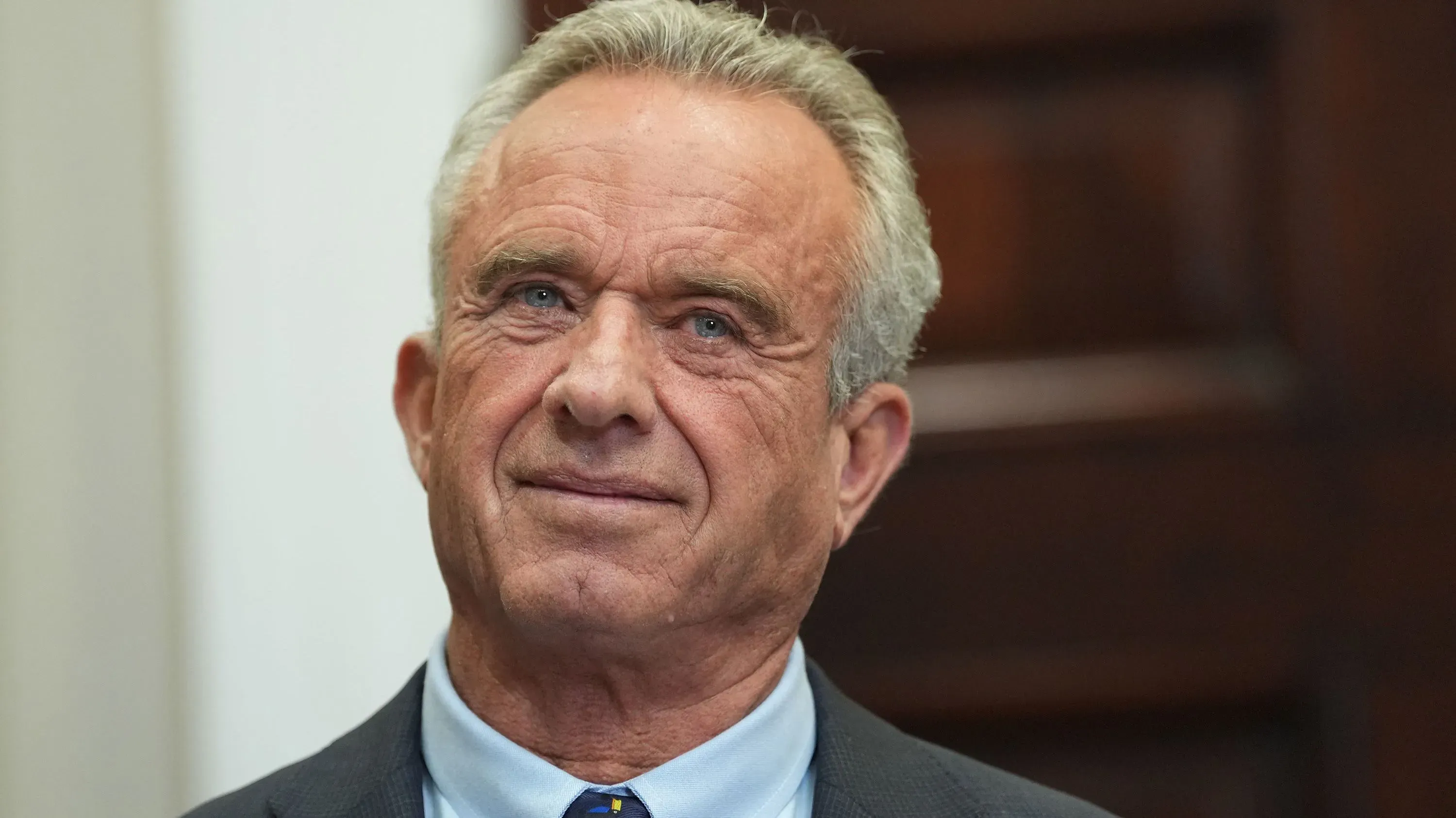 صورة لروبرت ف. كينيدي جونيور، وزير الصحة، يظهر فيها وهو يبتسم بينما يواجه الكاميرا، مع خلفية غير واضحة.