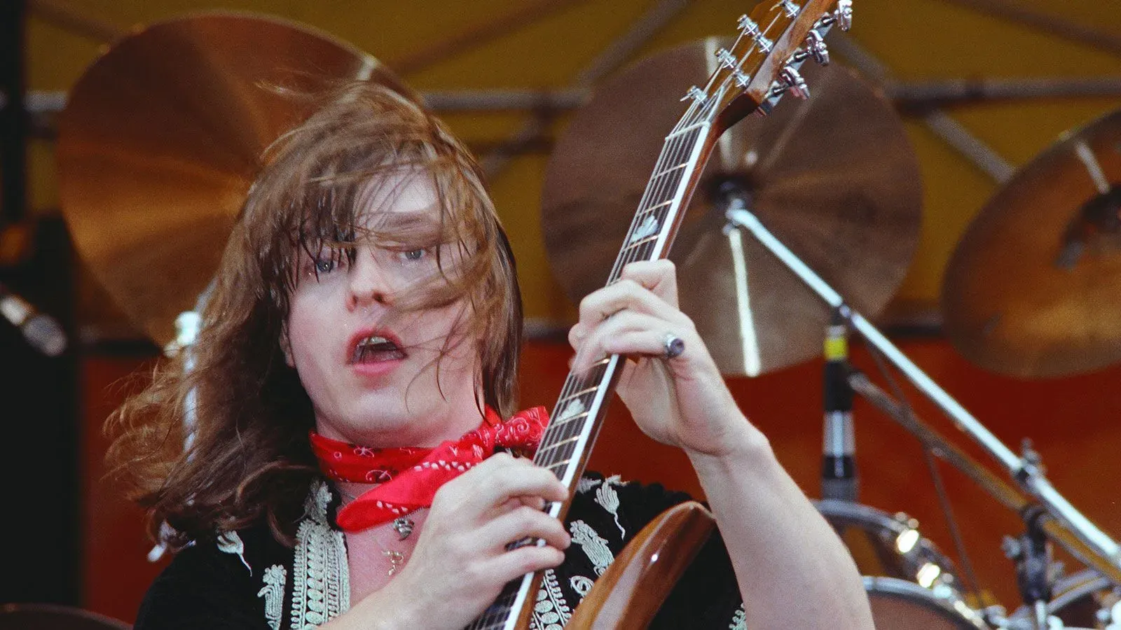 عازف الجيتار ريك ديرينجر يؤدي على المسرح، مع خلفية من الطبول، خلال ذروة مسيرته الموسيقية.