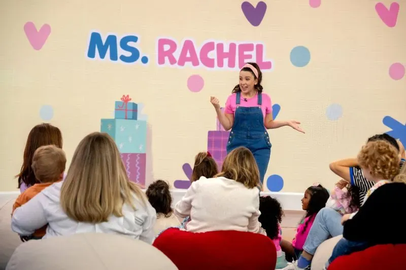 تظهر "الآنسة راشيل" في عرض للأطفال، حيث تتفاعل مع مجموعة من الأطفال الذين يجلسون أمامها، مما يعكس أهمية البرامج التعليمية في الأبوة.