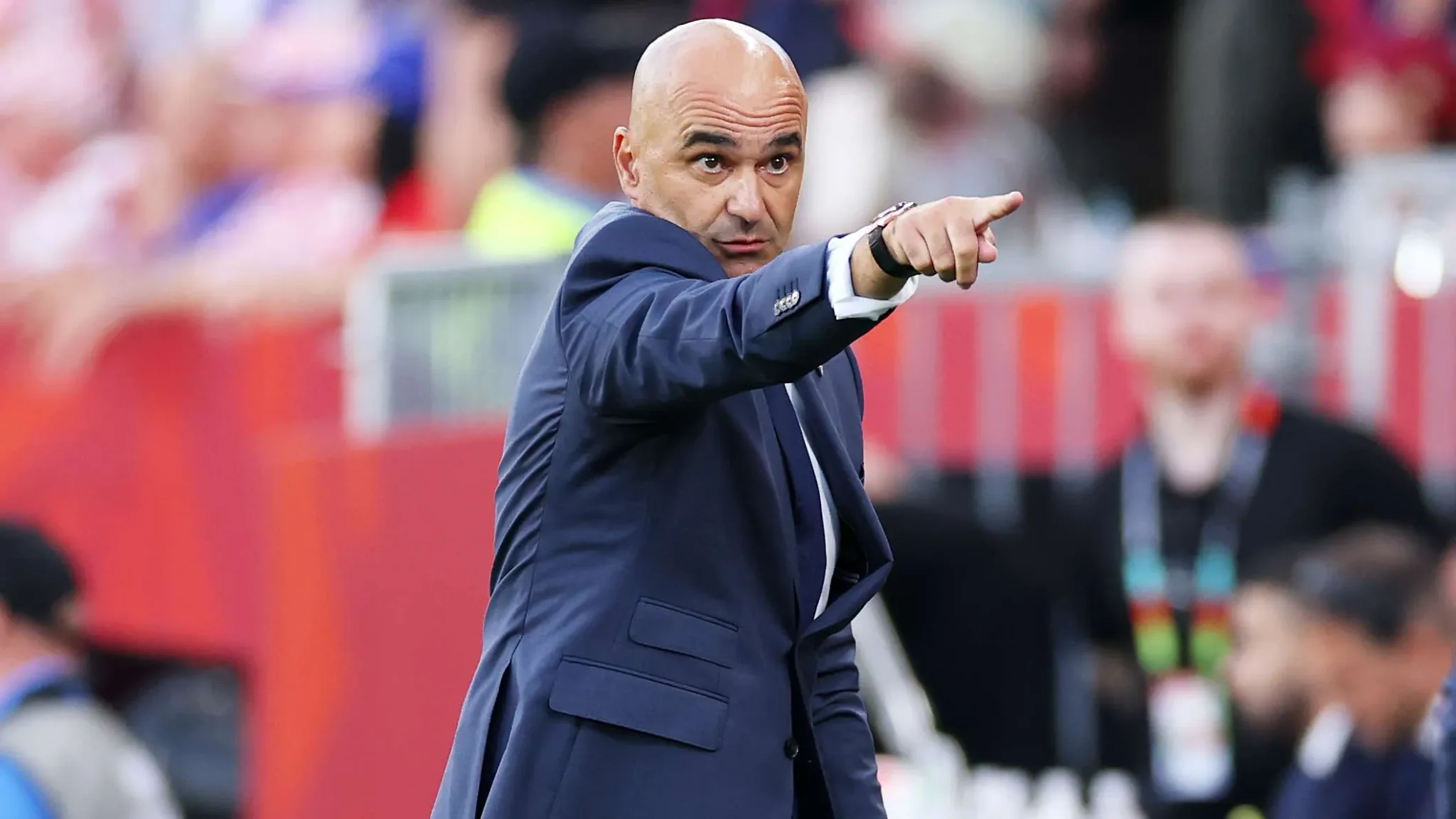 مدرب منتخب البرتغال Martinez يشير بحزم أثناء مباراة كأس العالم، مع خلفية جماهيرية حمراء تعكس أجواء التوتر والتحدي.