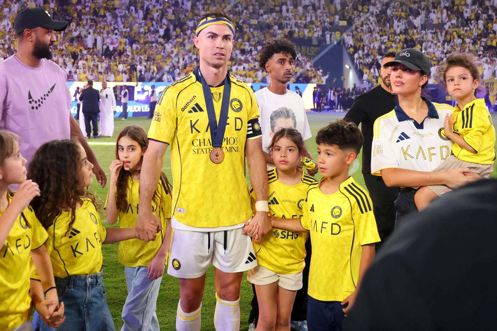 كريستيانو رونالدو بقميص النصر يحمل ميدالية وسط عائلته وأطفال يرتدون ألوان النادي في ملعب مكتظ بالجماهير بعد موسم حاسم في مسيرته مع الفريق.