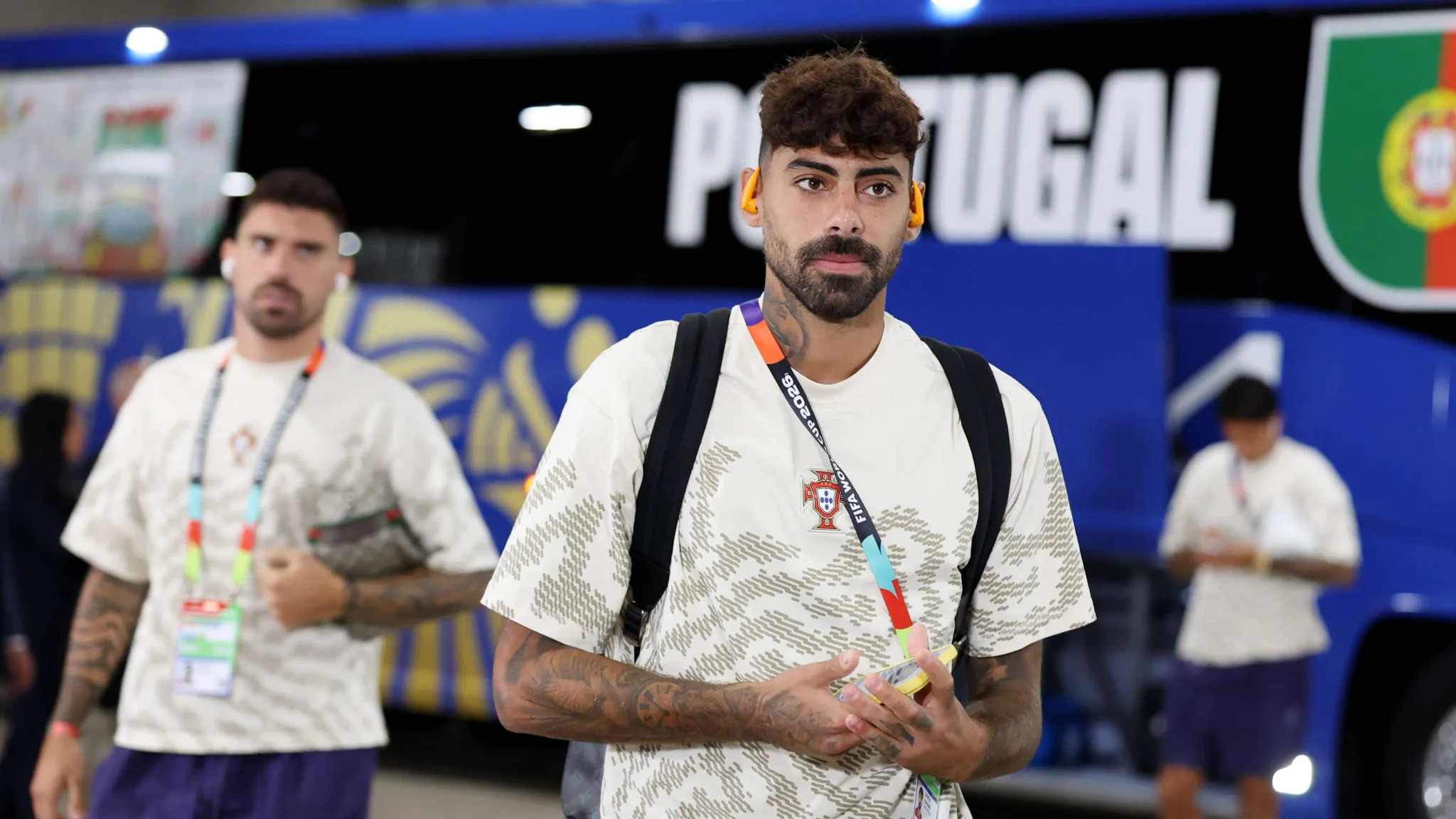لاعب كرة قدم برتغالي يرتدي زي منتخب بلاده، يظهر في خلفية حافلة تحمل شعار البرتغال، مع التركيز على استعدادات اللاعبين للمنافسات الدولية.