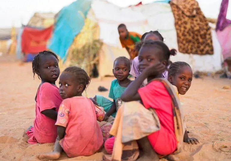 مجموعة من الأطفال يجلسون في مخيم للنازحين في السودان، تعكس ملامحهم المعاناة والأمل في ظل ظروف الحرب.