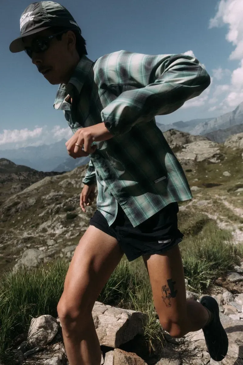 عداء يرتدي قميصاً مزخرفاً وشورتاً، يجري في منطقة جبلية خضراء، مع منظر جبلي في الخلفية، يعكس تنامي ثقافة الجري كرياضة اجتماعية.