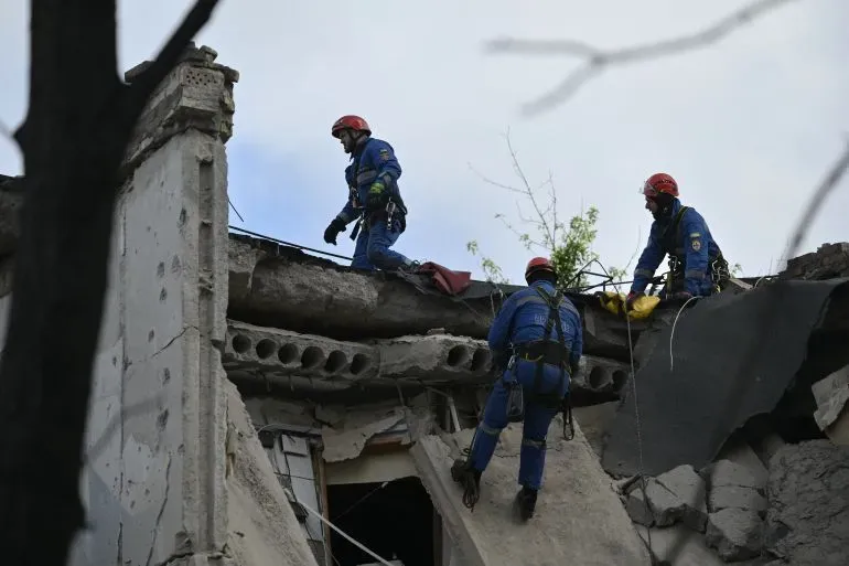 رجال إنقاذ يرتدون خوذات حمراء يقومون بعمليات البحث والإنقاذ على سطح مبنى مدمر في أوكرانيا بعد هجوم بطائرة مسيرة.