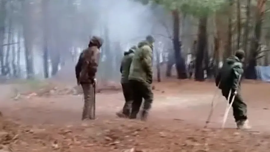 جنود روس مصابون يستخدمون العكازات في منطقة غابية، محاطون بدخان، يظهرون في حالة هروب من خطر محتمل.