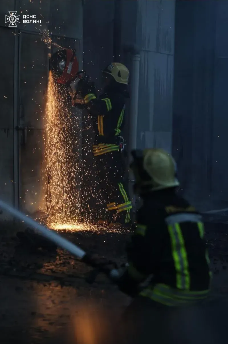 رجال الإطفاء يعملون في موقع حادث، يستخدم أحدهم منشارًا كهربائيًا لإزالة الحطام بينما يراقب الآخر، مع تصاعد الشرر.