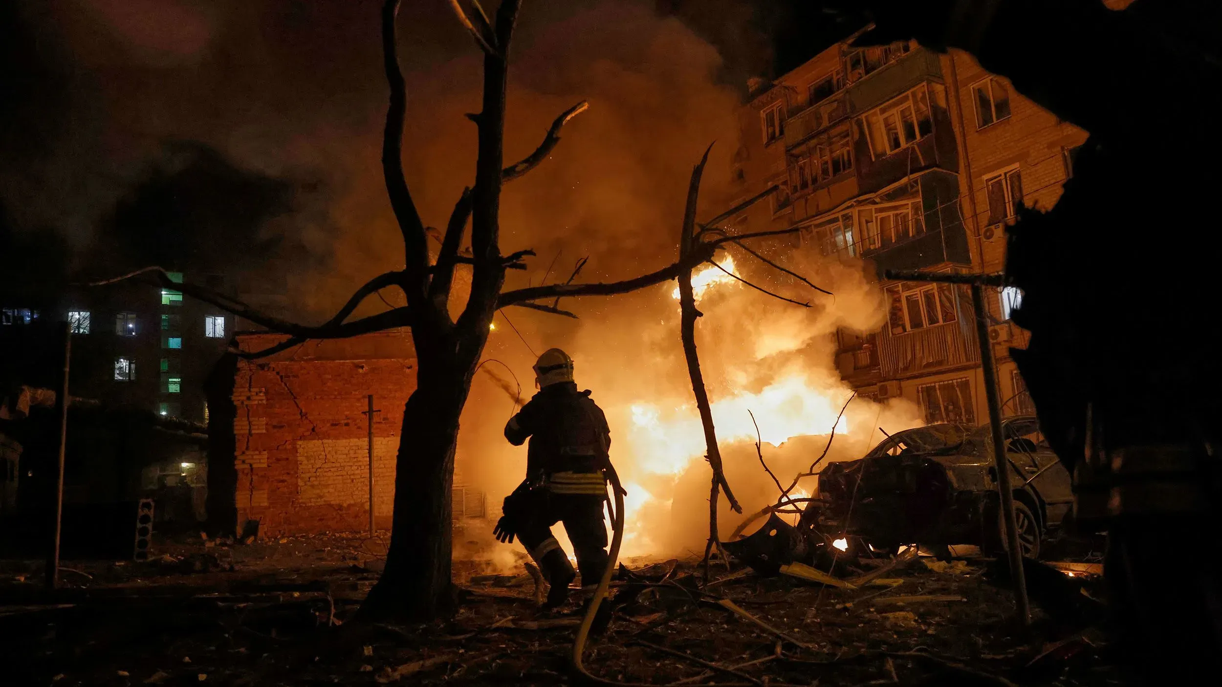 مشهد لرجال الإطفاء في موقع انفجار ليلي، حيث تتصاعد النيران والدخان من مبنى مدمر، مما يعكس تأثير الصراع في أوكرانيا.