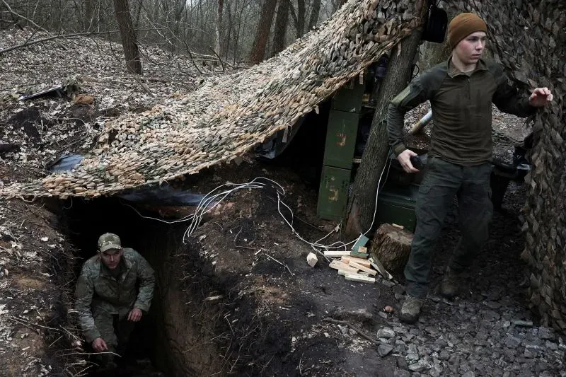 جنود أوكرانيون يعملون في موقع عسكري تحت غطاء تمويهي في غابة، مع وجود خندق يستعدون لمواجهة هجمات روسية محتملة.