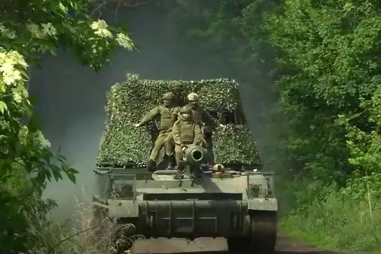 جنود أوكرانيون يجلسون على دبابة مغطاة بأغصان الأشجار خلال تحركهم في منطقة غابية، مما يعكس الوضع العسكري الحالي في أوكرانيا.