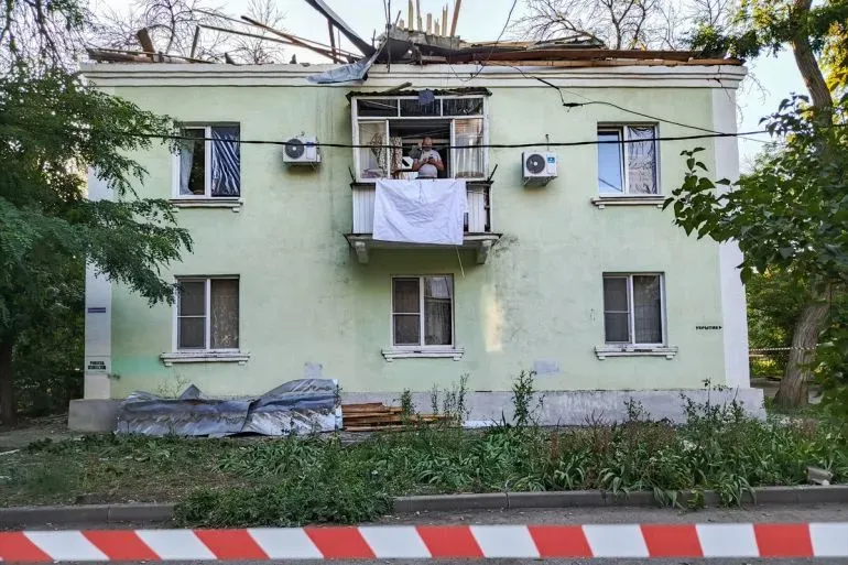أضرار واضحة في مبنى سكني بأوكرانيا بعد هجوم، مع شخص يقف على الشرفة. يظهر السقف المتضرر والنوافذ المكسورة.