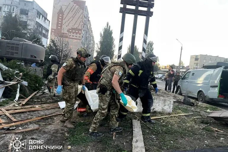 فرق الإنقاذ تحمل جثثًا من موقع قصف في أوكرانيا، مع وجود مبانٍ مدمرة في الخلفية، مما يعكس آثار الحرب المستمرة.