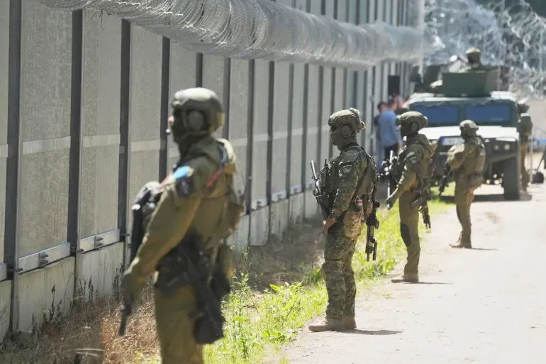 جنود مسلحون يقفون أمام جدار محصن، مع وجود أسلاك شائكة في الأعلى، خلال زيادة التوترات الأمنية في المنطقة.