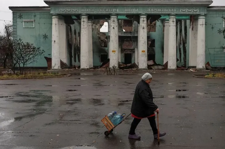 امرأة مسنّة تسير على الرصيف بجوار مبنى مدمّر في منطقة زابوريجيا، تعكس آثار الصراع المستمر في أوكرانيا.