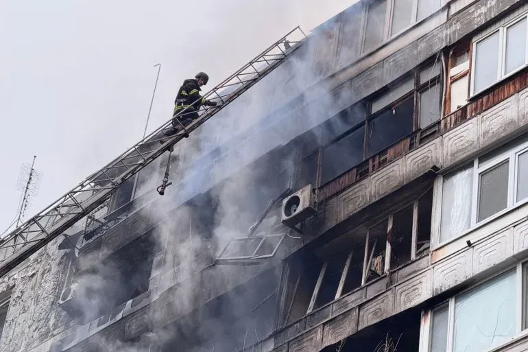 رجال الإطفاء يتسلقون سلمًا لإنقاذ الأرواح من مبنى متضرر جراء الهجمات الروسية، مع تصاعد الدخان من النوافذ المحطمة.