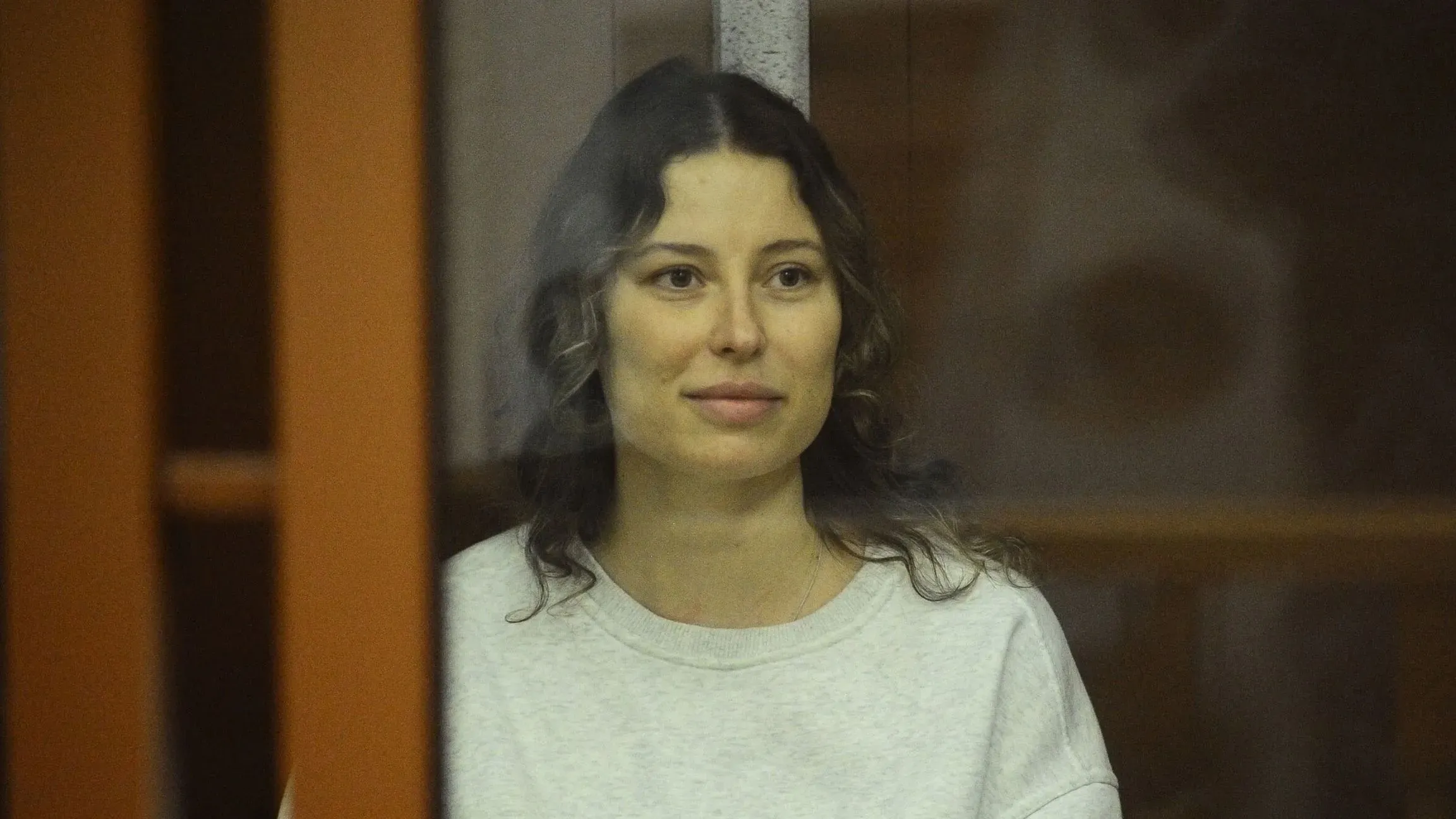 كسينيا كاريلينا، الأمريكية الروسية، تظهر مبتسمة خلف زجاج أثناء محاكمتها، بعد إطلاق سراحها من السجن في روسيا.