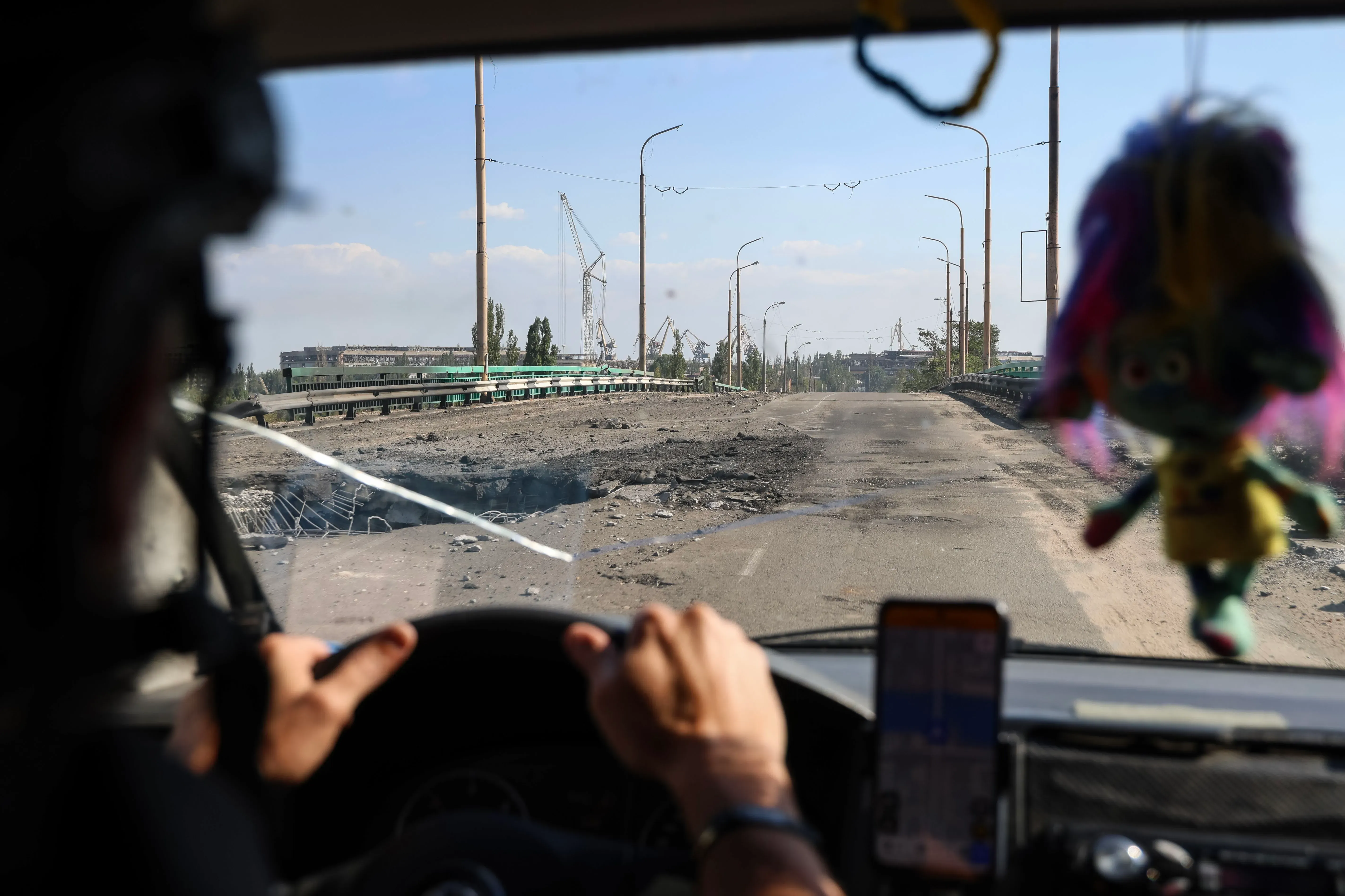 صورة تظهر مشهدًا من داخل مركبة أثناء القيادة على طريق تضرر بشدة في خيرسون، مع آثار دمار واضحة ودمار حوله، مما يعكس تأثير الغارات الجوية.