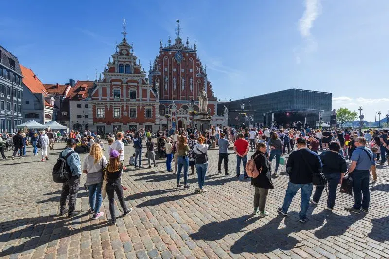 ساحة مزدحمة في مدينة تاريخية، حيث يتجمع الناس أمام مبنى قديم جميل، مع أجواء مشمسة تعكس النشاط السياحي في أوروبا.