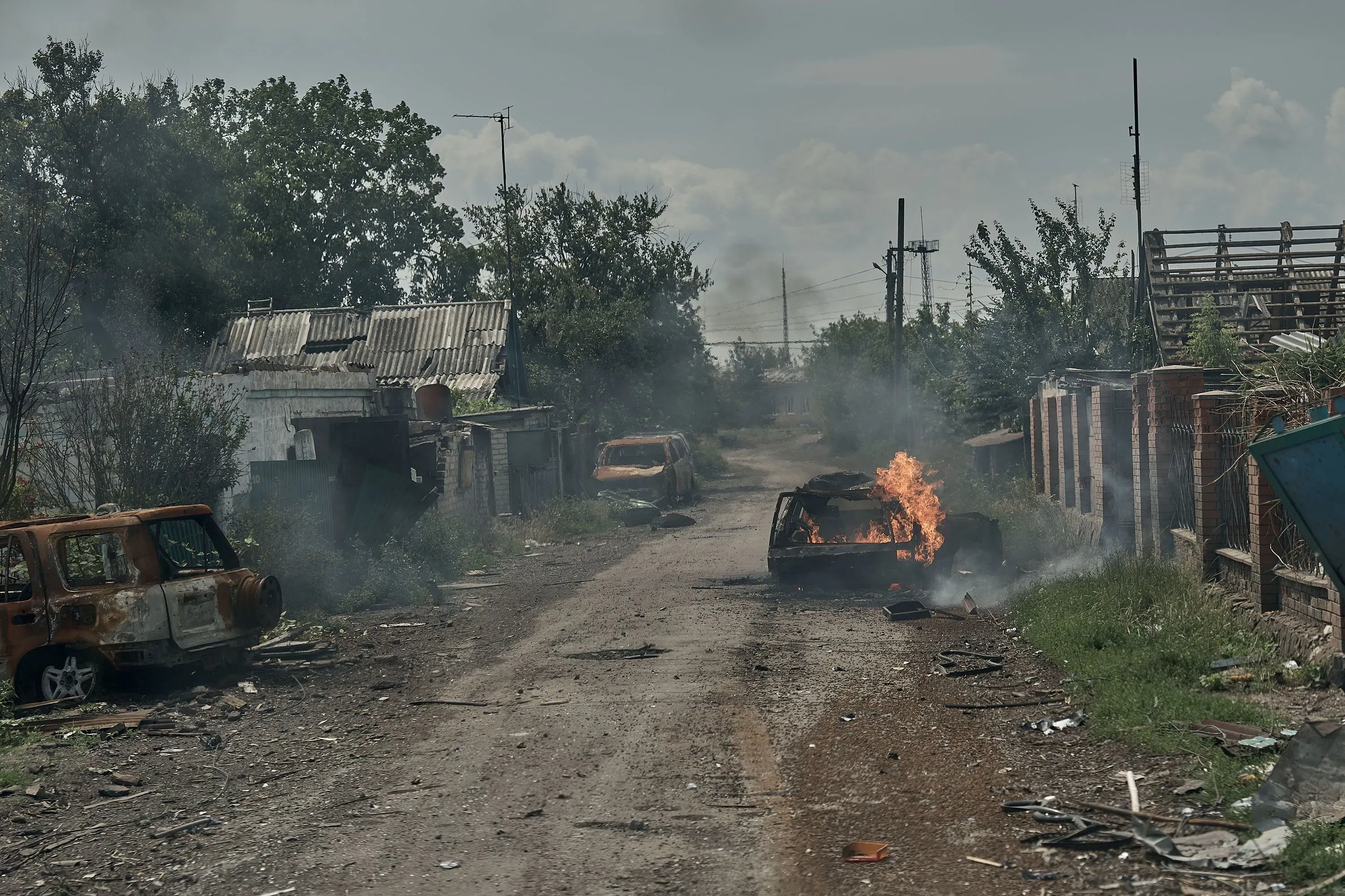 شارع مدمر في بلدة بوكروفسك، تظهر فيه سيارات محترقة وأدخنة تتصاعد، مما يعكس آثار الصراع المستمر في شرق أوكرانيا.