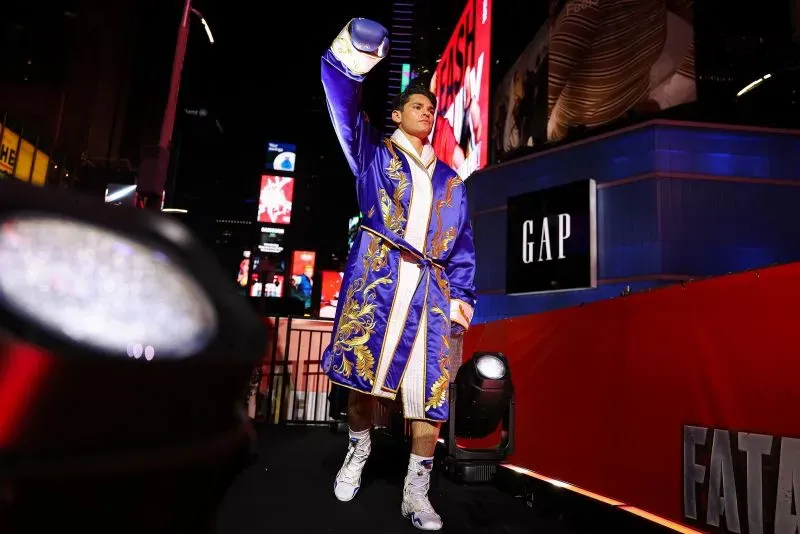 ريان غارسيا يرتدي رداءً مزينًا بألوان زاهية ويحيي الجمهور قبل نزال في ساحة تايمز سكوير، وسط أضواء الإعلانات الساطعة.