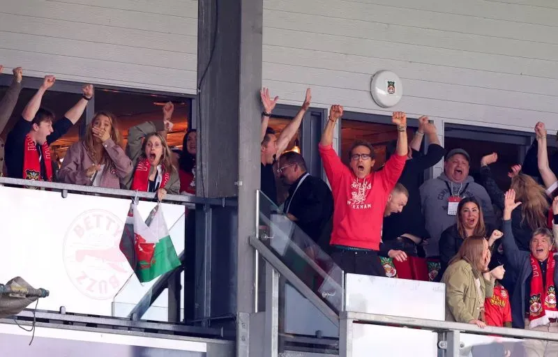 جماهير نادي ريكسهام تحتفل بفوز الفريق في مباراة حاسمة، مع تعبيرات الفرح والحماس في المدرجات.