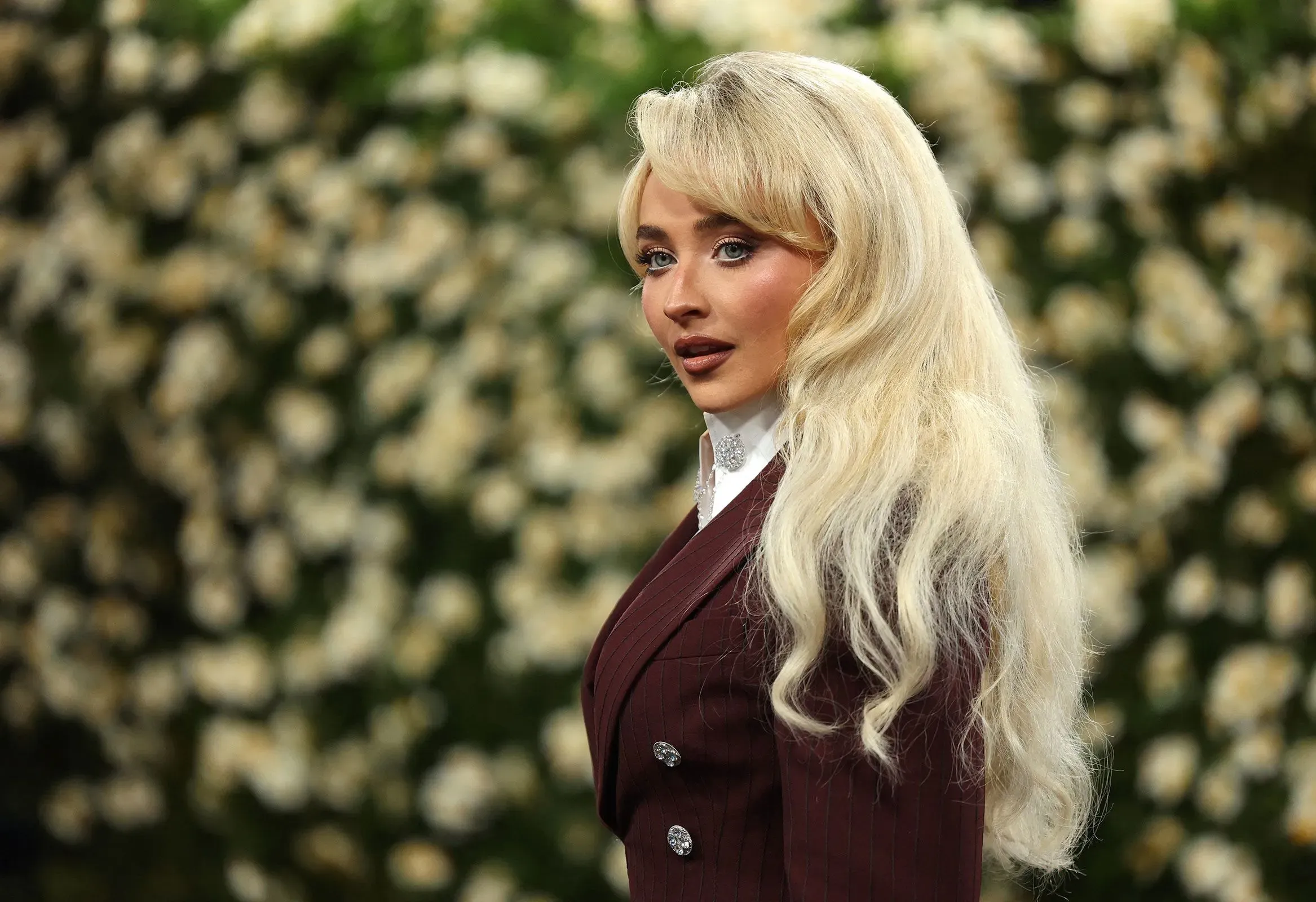 سابرينا كاربنتر تتألق في فستان أنيق، مع خلفية من الزهور، تعبر عن استيائها من استخدام أغنيتها في فيديو للبيت الأبيض.