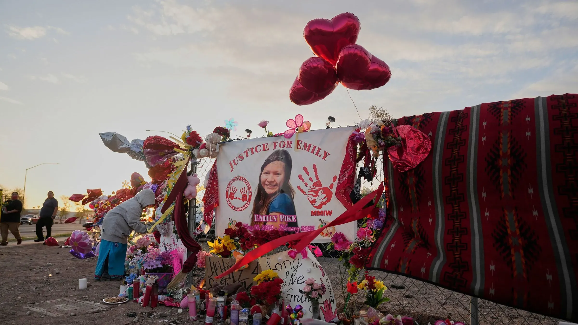 موقع تذكاري لإيميلي بايك، يتضمن لافتة مكتوب عليها "العدالة لإيميلي"، وزهور، وقلوب حمراء، وأضواء الشموع، تعبيرًا عن الحداد والدعوة لإنهاء العنف ضد النساء.