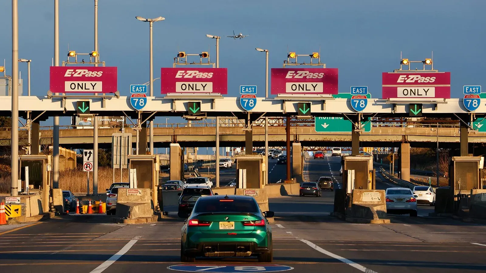 ممر رسوم مرور مع لافتات "EZPass ONLY" تشير إلى ضرورة استخدام بطاقة EZPass للدفع، مع حركة مرور نشطة في الخلفية.