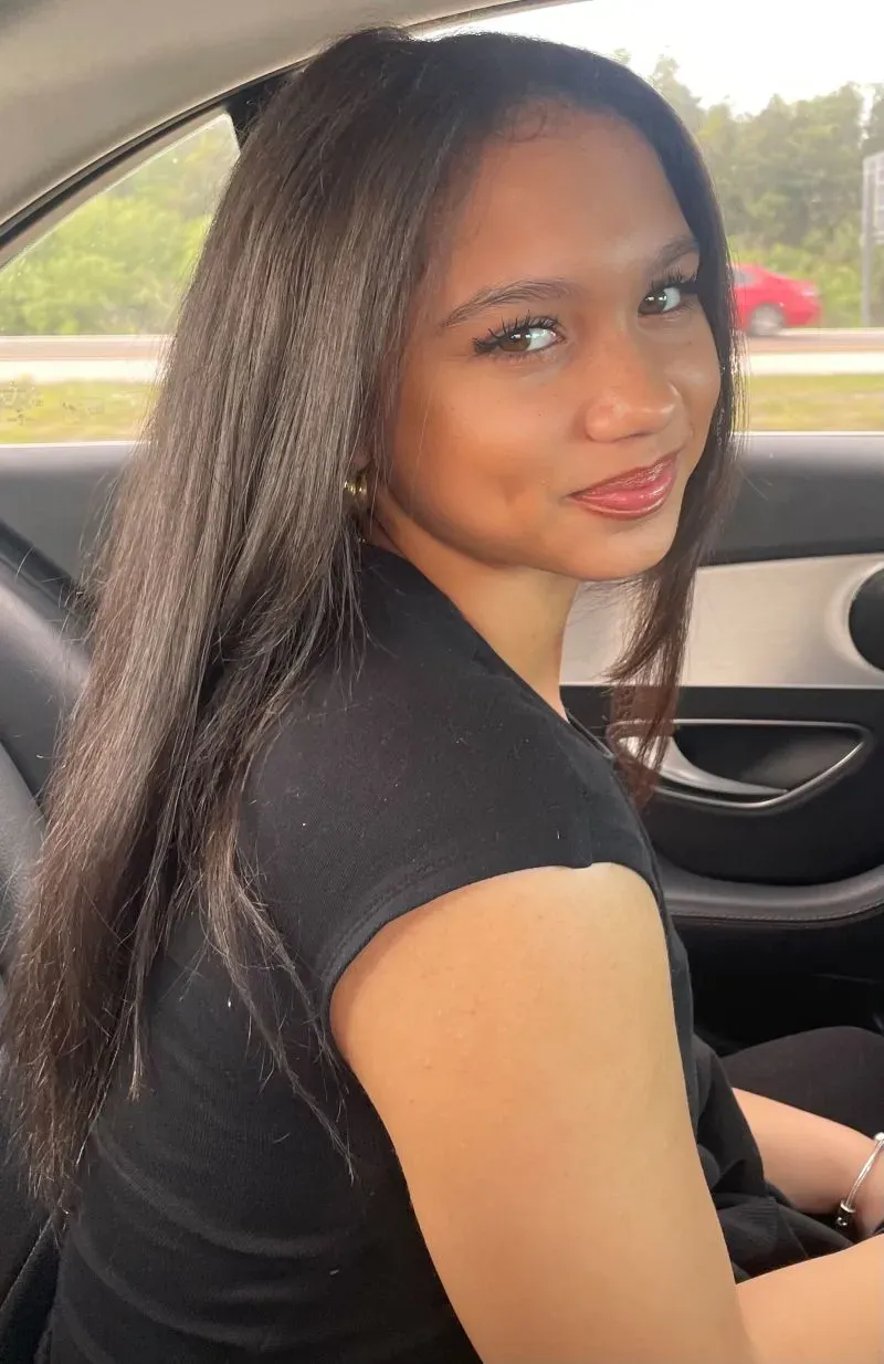 صورة لفتاة شابة مبتسمة تجلس في سيارة، تعكس روح الأمل بعد حادث صدمها بحافلة مدرسية.