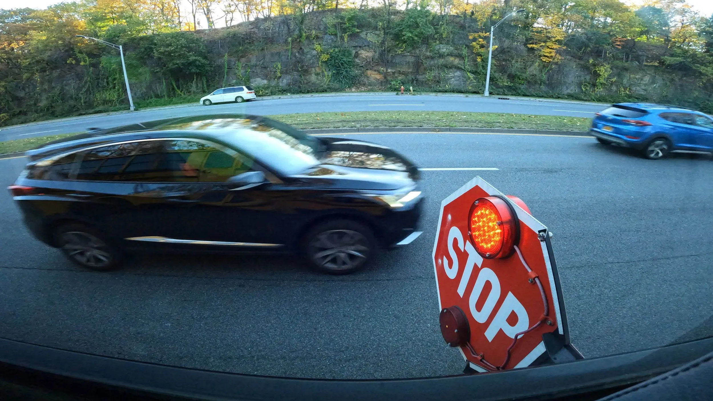 سيارة سوداء تتجاوز علامة توقف حمراء مضاءة على جانب حافلة مدرسية، مما يبرز مخاطر المرور حول محطات الحافلات.