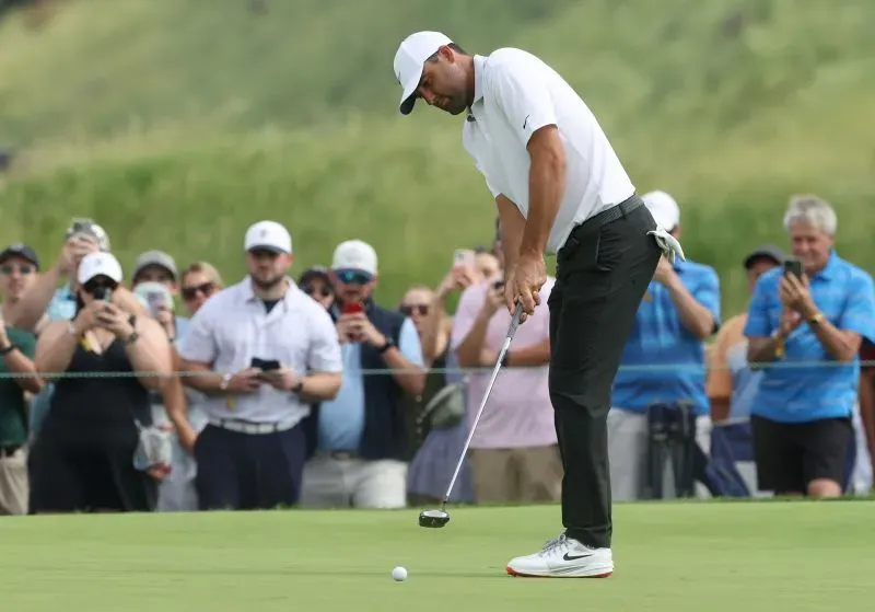 سكوتي شيفلر يضع الكرة في حفرة خلال بطولة جولف، مع جمهور يراقب من خلفه في نادي أوكمونت كونتري.