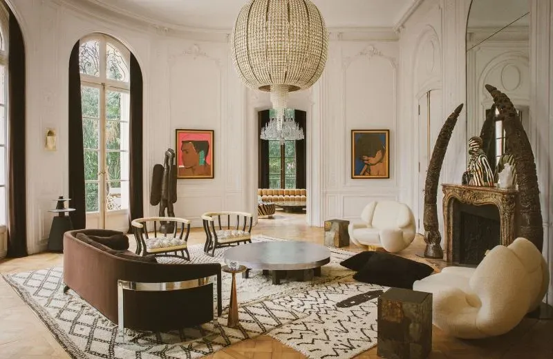 غرفة معيشة أنيقة في منزل ليني كرافيتز في باريس، تتميز بديكورات فنية وأثاث عصري، مع ثريا كبيرة ونوافذ تطل على الحديقة.